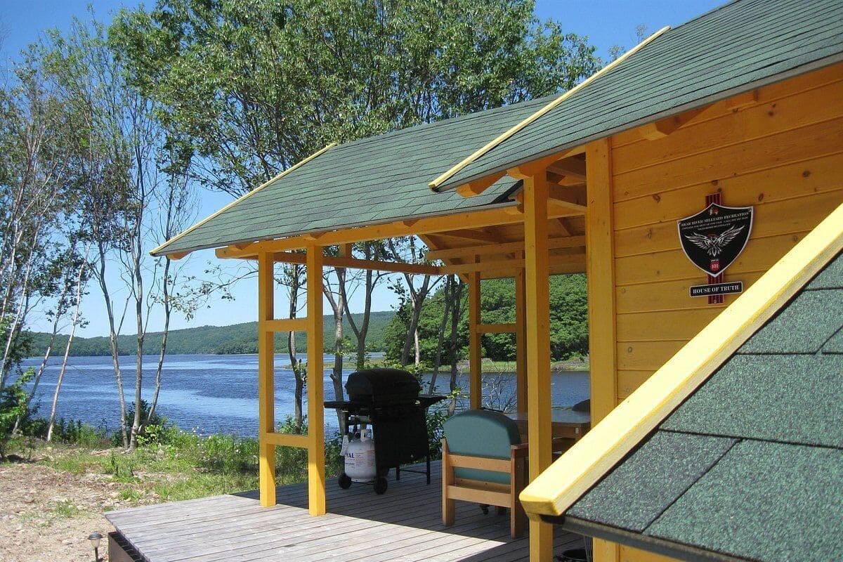 Eine Holzhütte mit überdachter Veranda, Grill und Stuhl.