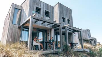 A modern wooden house with a covered porch where two people are sitting at a table.