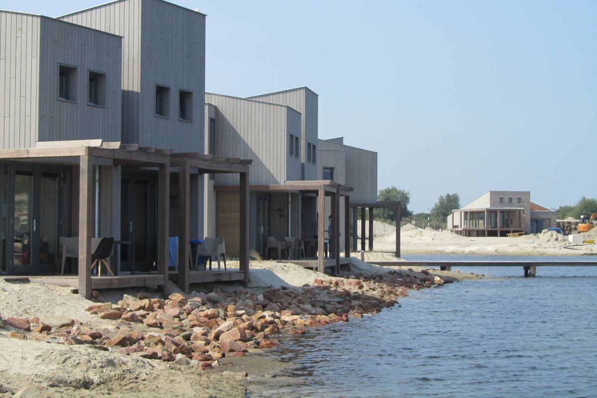 Un edificio moderno con diversi piani e ampie finestre, situato vicino a un corpo d'acqua con un litorale roccioso.