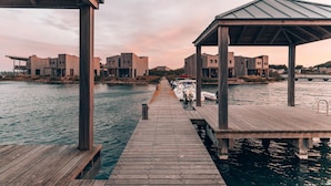 Un muelle de madera que conduce a un muelle con barcos, rodeado de edificios modernos con un estilo arquitectónico uniforme.