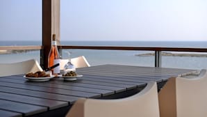 Una mesa con una botella de vino, una copa y un plato de aceitunas, con vistas a un cuerpo de agua.