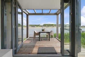 Et moderne udendørs opholdsområde med et bord og stole, med udsigt over vandet.