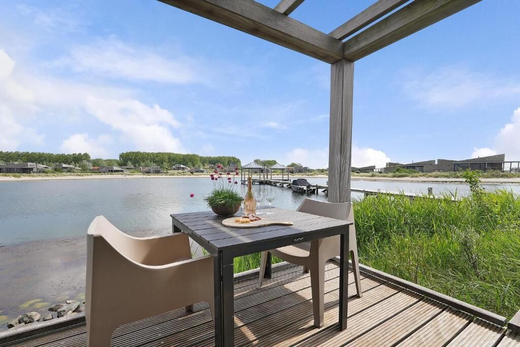 An outdoor seating area with a table and chairs overlooking a body of water, with buildings in the background.