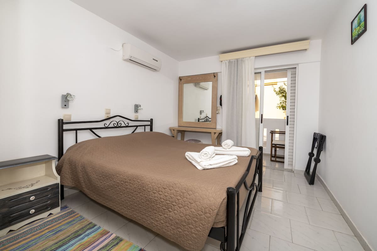 Un dormitorio con cama, mesita de noche, espejo y vistas al exterior.