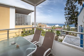 A balcony with a glass table and chairs, overlooking a coastal view with buildings and a clear sky. - Villa Giorgos (Kos)