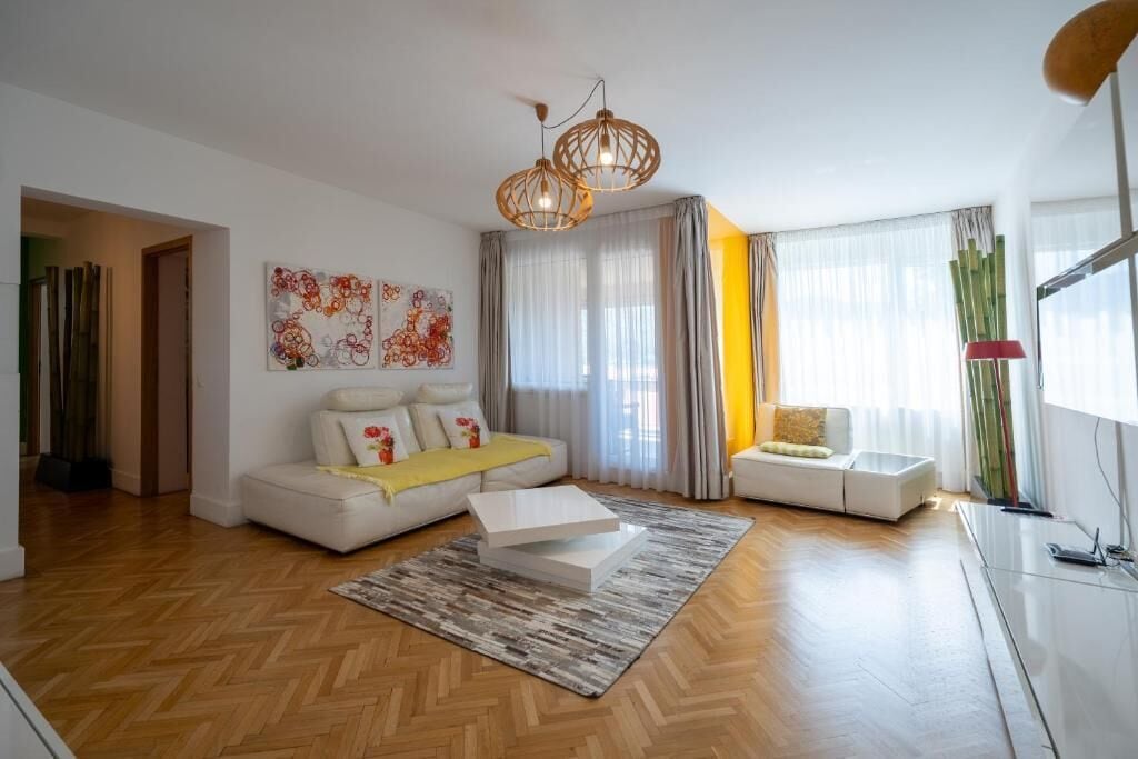 A modern living room with a sofa, a coffee table, and a rug. There is a painting on the wall and a lamp on a table.