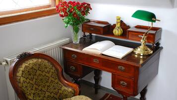 Ein Holztisch mit einem Buch, einer grünen Schreibtischlampe und einer Vase mit roten Blumen.