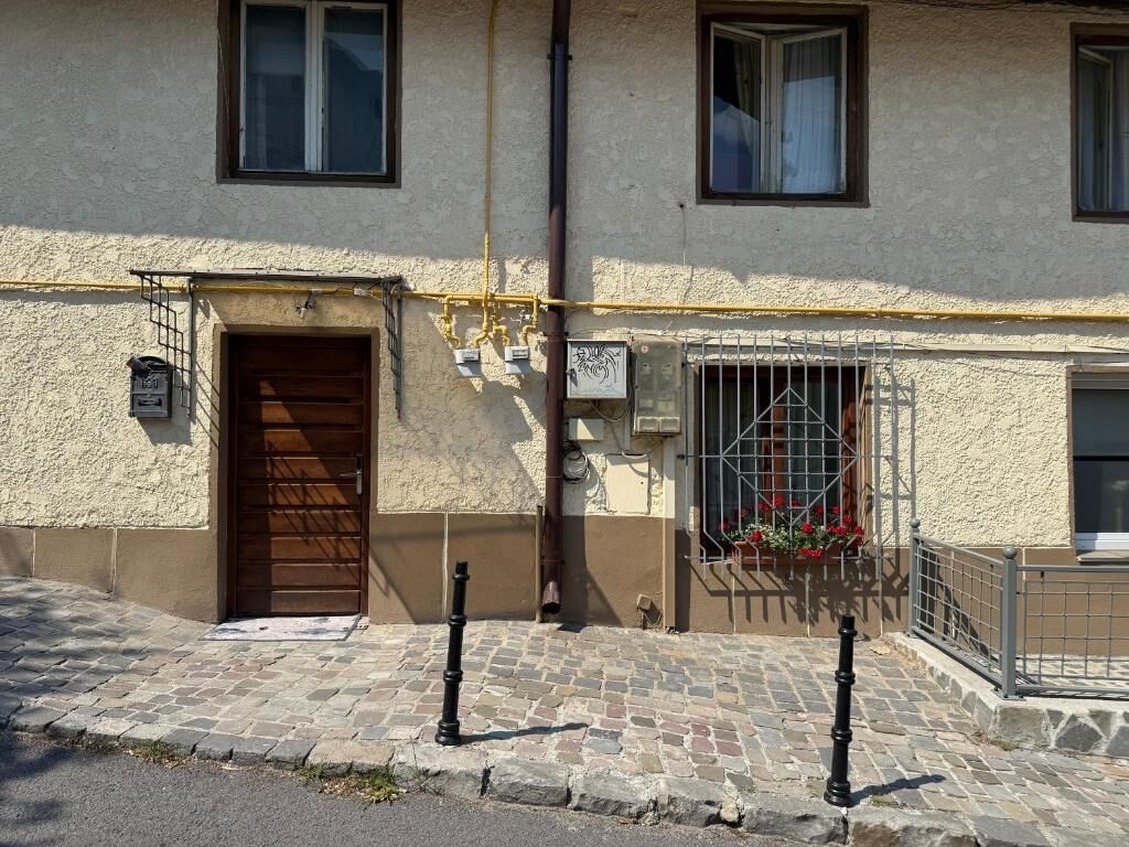 A building with a wooden door, a window with a metal grill, and a small balcony with flowers.
