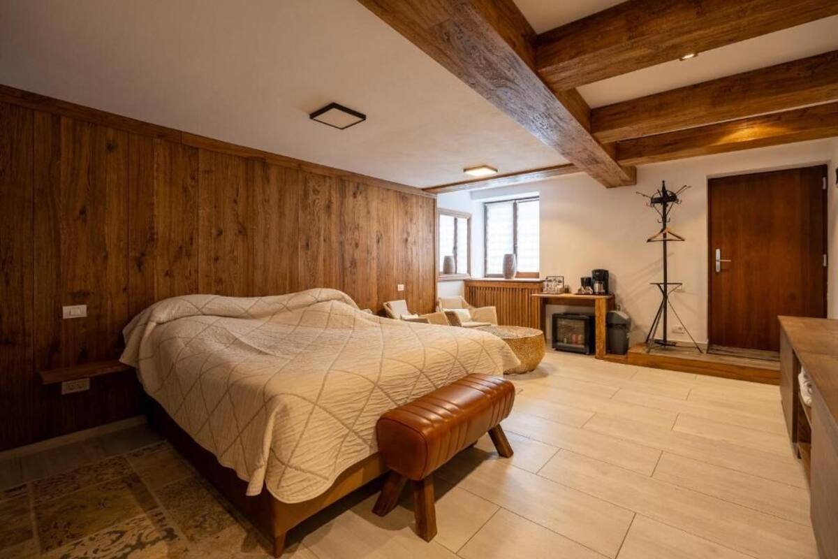 Un dormitorio con una cama grande, paredes de madera, un banco y una pequeña mesa con una lámpara.