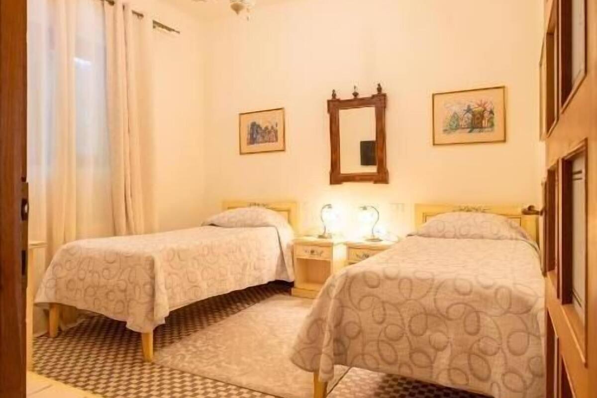 Habitación de hotel con dos camas, una araña de cristal, suelo a cuadros y un espejo en la pared.