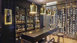 Un espace bar doté d’un comptoir en granit poli, de luminaires suspendus en laiton et d’un mur entièrement recouvert de bouteilles de vin.