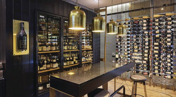 Un espace bar doté d’un comptoir en granit poli, de luminaires suspendus en laiton et d’un mur entièrement recouvert de bouteilles de vin.