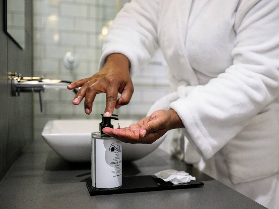 Une personne vêtue d’un peignoir blanc utilise un distributeur de savon liquide sur le comptoir d’une salle de bain.