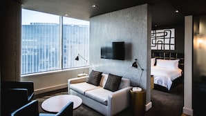 Une chambre d’hôtel moderne dotée d’une grande fenêtre, d’un canapé, d’un lit et d’un téléviseur à écran plat fixé au mur.