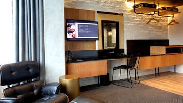 Una habitación de hotel moderna con un escritorio de madera, un sillón de cuero negro, un sofá de cuero negro y un televisor montado.
