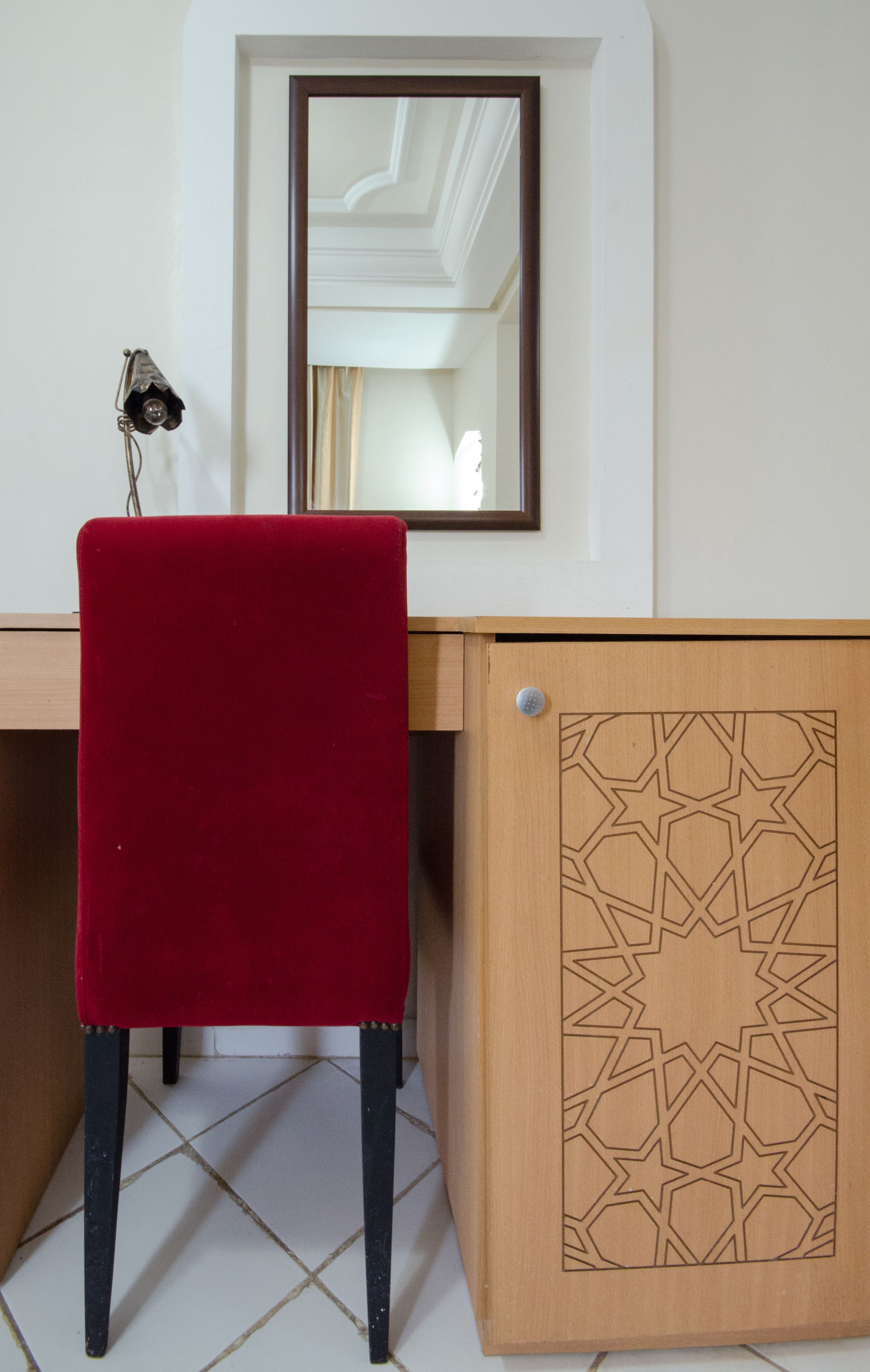 Une pièce avec un bureau en bois, une chaise rouge et un meuble orné d’un motif géométrique.