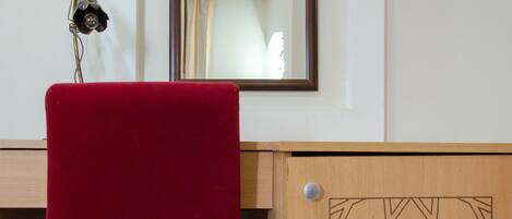 Une pièce avec un bureau en bois, une chaise rouge et un meuble orné d’un motif géométrique.