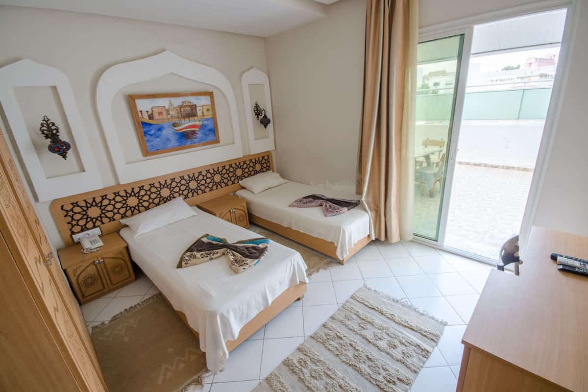A hotel room with two beds, a painting on the wall, a desk, and a view of the outside.