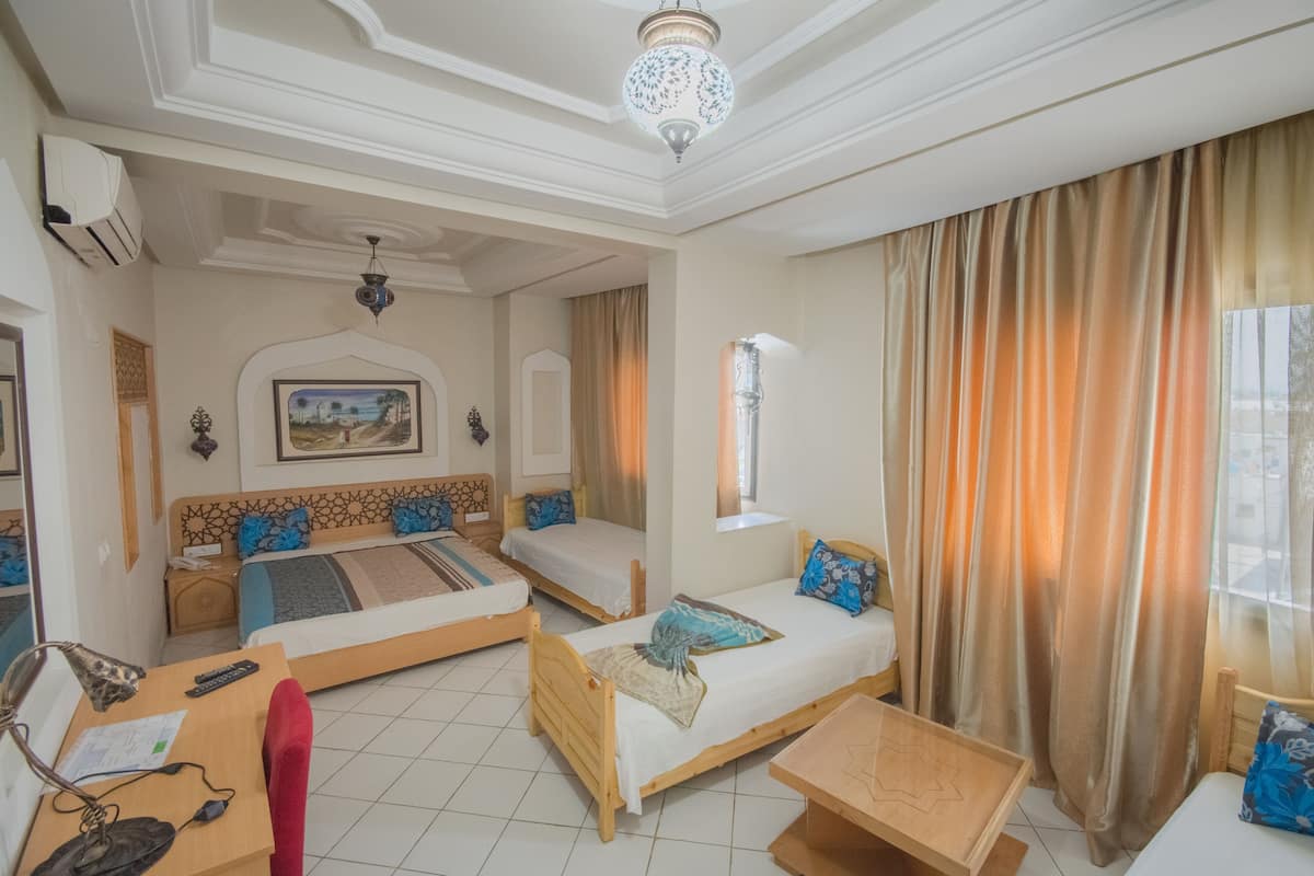 A hotel room with two beds, a desk, a chair, a small table, and a large window with curtains.