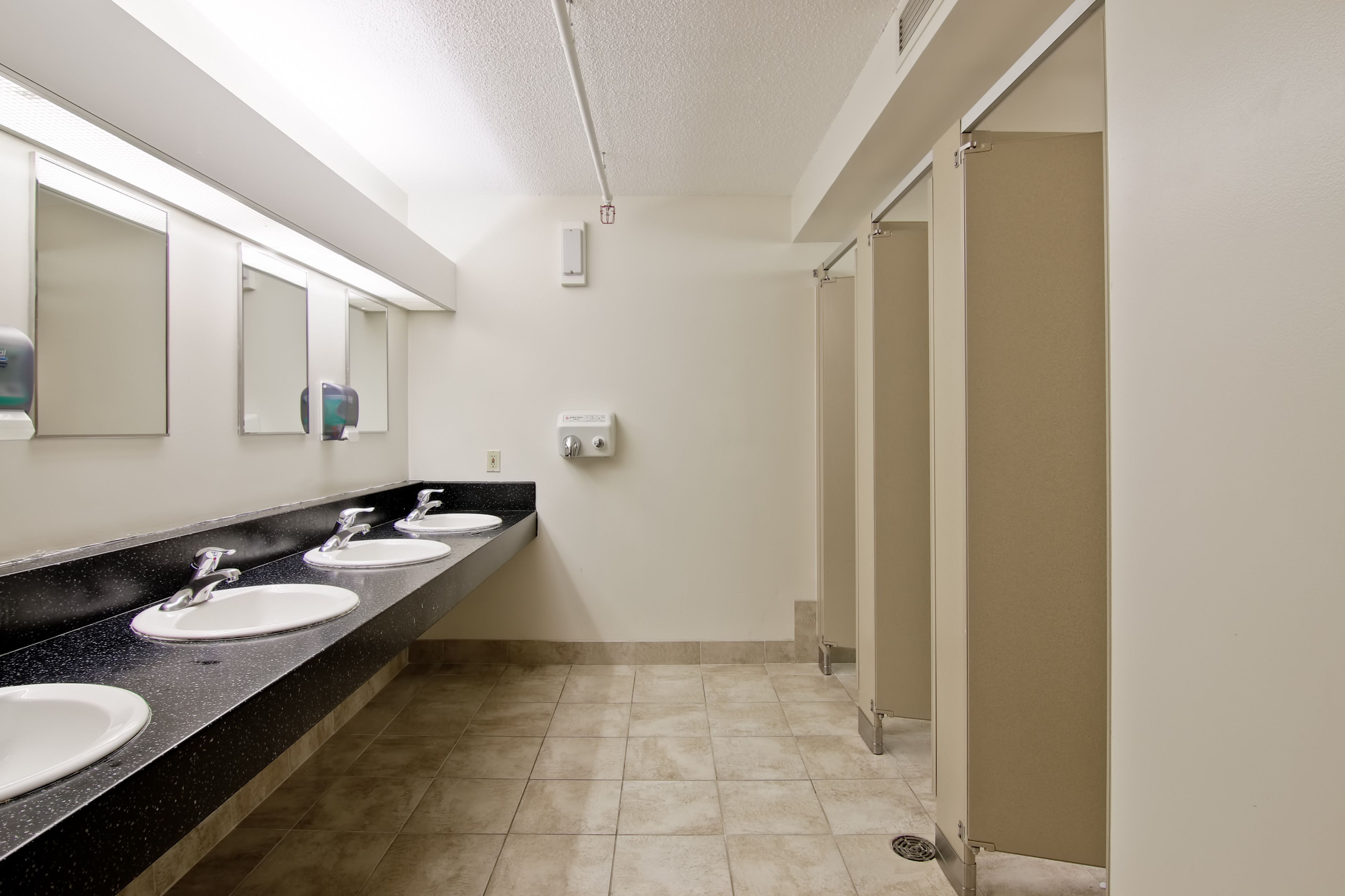 A public restroom with three sinks, a hand dryer, and a paper towel dispenser.
