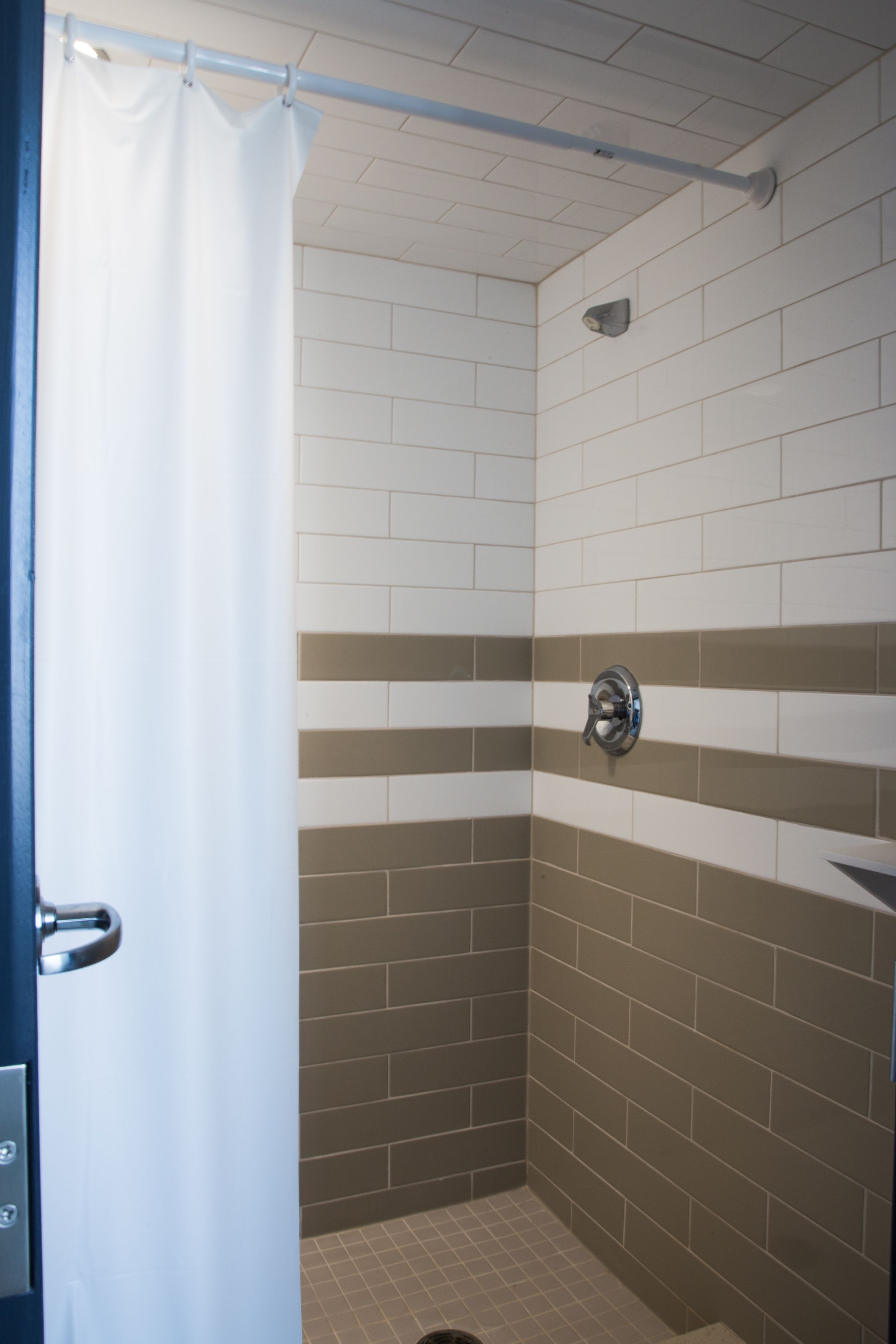 A shower area with white and beige tiles, a showerhead, and a curtain.