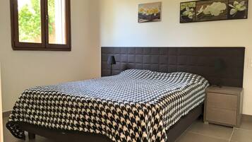 A bedroom with a houndstooth-patterned bedspread, a dark headboard, a bedside table with a lamp, and two wall-mounted flower paintings.