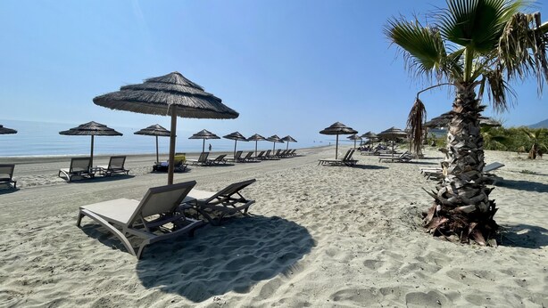 Uma praia com espreguiçadeiras e guarda-sóis de palha.