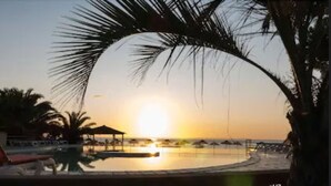 Vista da piscina com pôr do sol, palmeiras e uma cadeira de lounge.