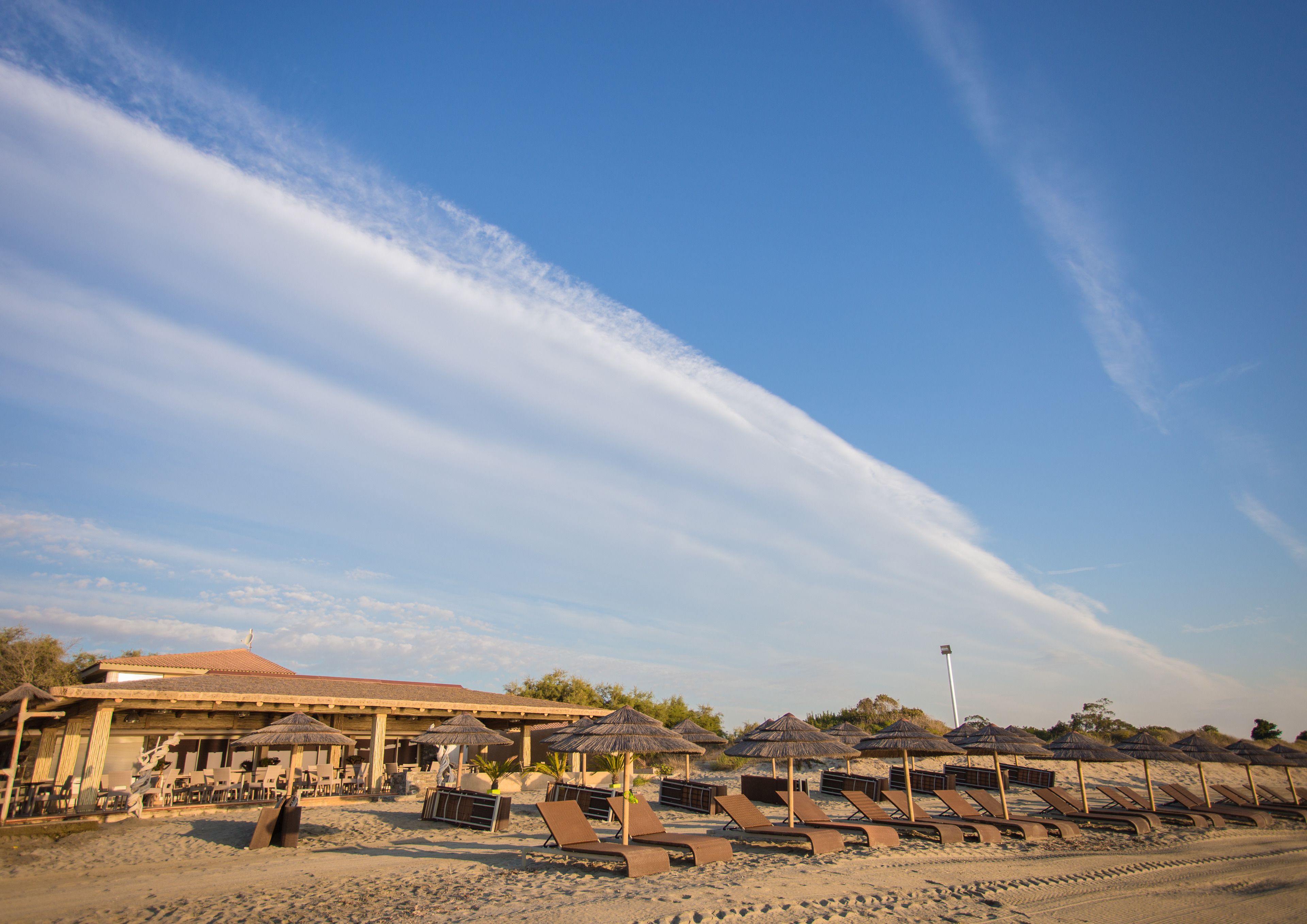 A beachside resort with sun loungers, thatched umbrellas, and a building with a tiled roof.