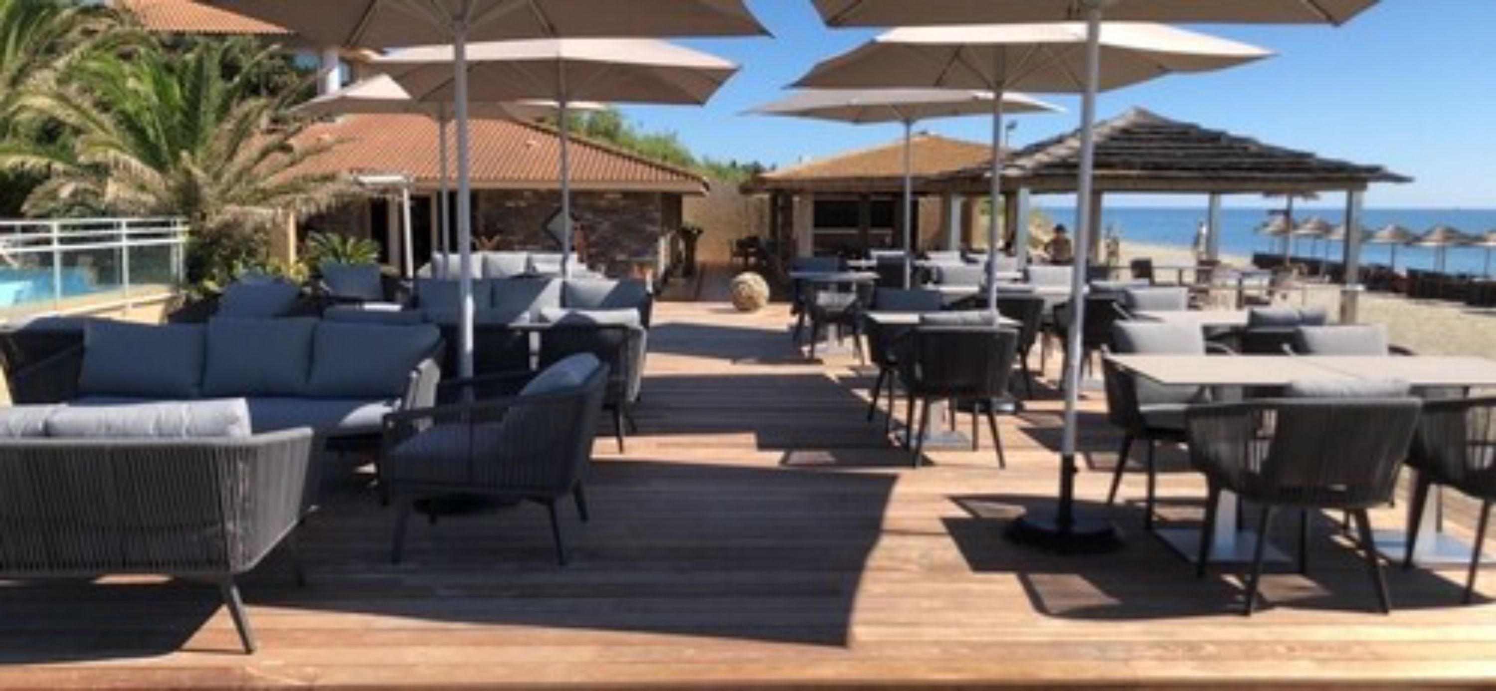 An outdoor deck with seating and umbrellas, overlooking a pool and beach area.