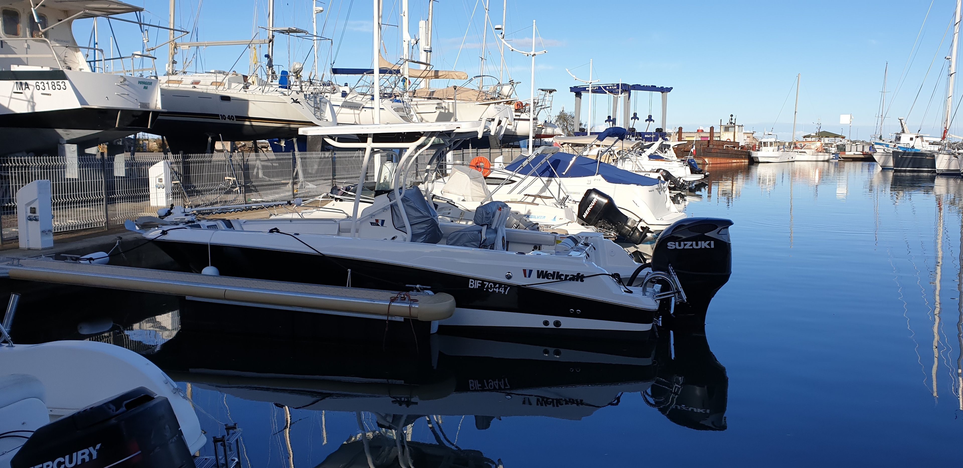 Un puerto deportivo con varias embarcaciones amarradas, incluyendo un velero en buen estado con motor Suzuki.