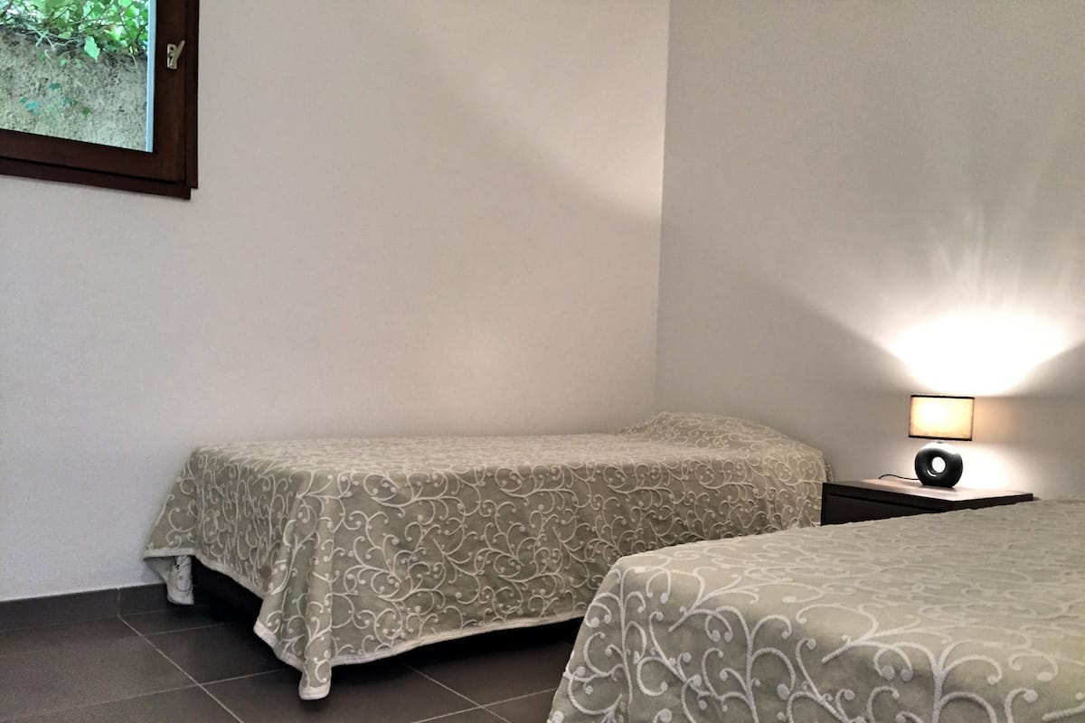 Hotellihuone, jossa on kaksi sänkyä, yöpöytä lampun kanssa ja seinällä oleva kehystetty kuva.