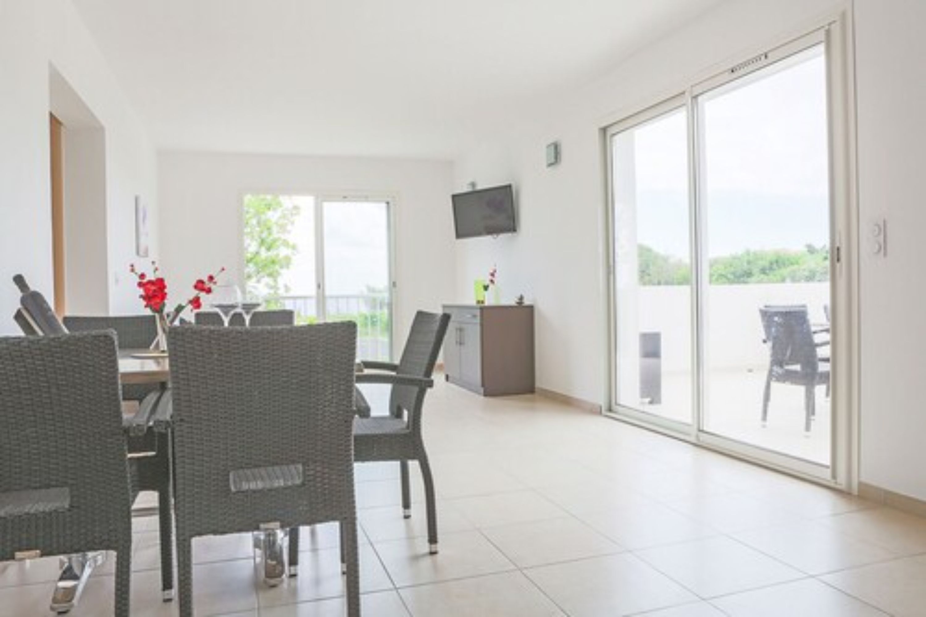 A spacious room with a dining area, a television mounted on the wall, and a sliding glass door leading to an outdoor area.