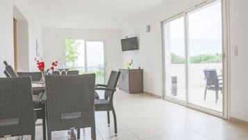 A spacious room with a dining area, a television mounted on the wall, and a sliding glass door leading to an outdoor area.