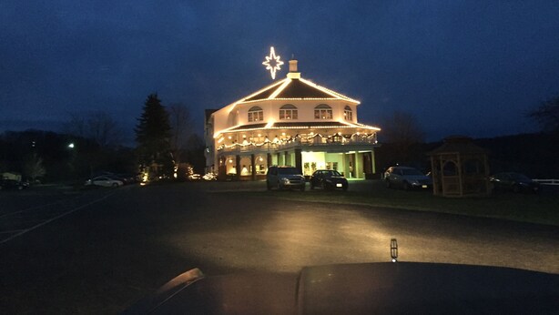A building with a star on top, a covered porch, and cars parked in front. - Inn at Amish Door (Wilmot)