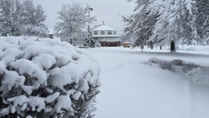 A snow-covered landscape with a large building in the background, surrounded by trees and a clear sky. - Inn at Amish Door (Wilmot)