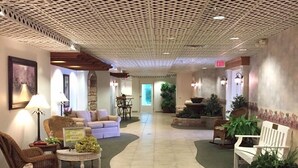 A spacious lobby with a high ceiling featuring a geometric pattern, a reception area with a sign, and several seating areas with potted plants. - Inn at Amish Door (Wilmot)