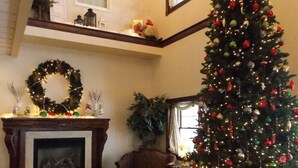 A cozy living room with a fireplace, a large Christmas tree, and a chandelier. - Inn at Amish Door (Wilmot)