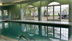 A swimming pool with clear water, surrounded by large windows offering views of the outdoors. - Inn at Amish Door (Wilmot)