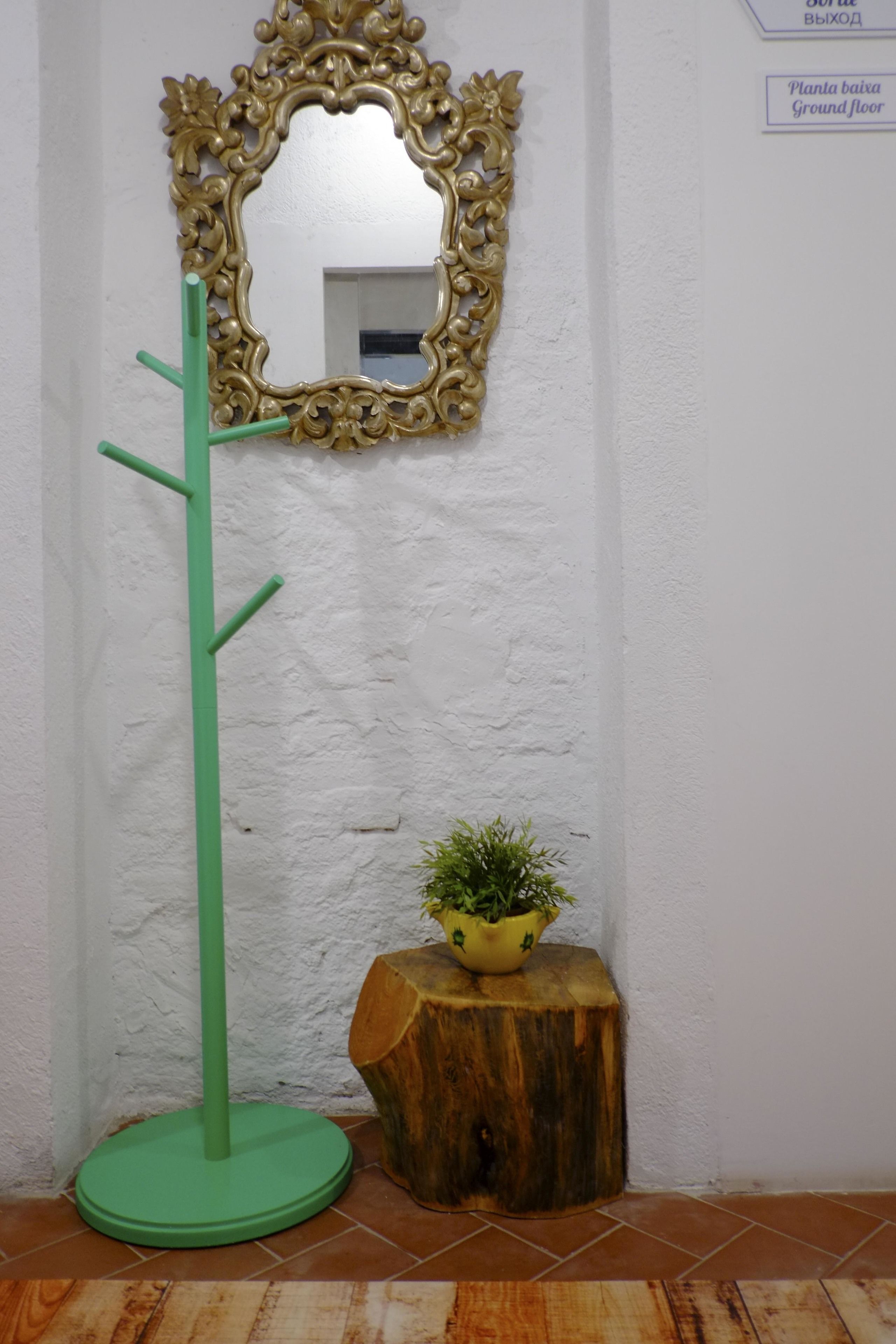 Una lámpara de pie verde con un espejo, un taburete de madera con una planta, y un cartel que indica planta baja.