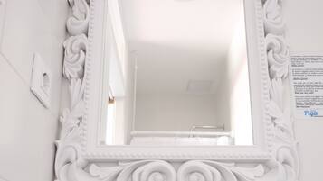 A bathroom with a white ornate mirror, a sink with two clear glasses, and two tubes of sea salt.