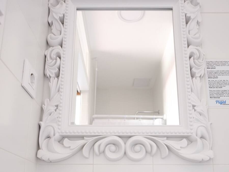 A bathroom with a white ornate mirror, a sink with two clear glasses, and two tubes of sea salt.