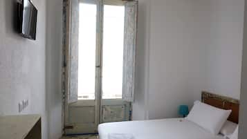 A bedroom with a bed, a TV mounted on the wall, and a door with a view to the outside.