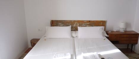 A double bed with white linens, a wooden headboard, a bedside table with a lamp, and a remote control on the bed.