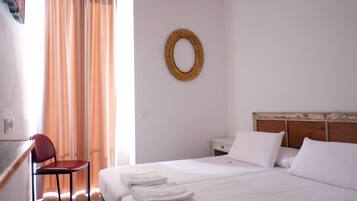 Habitación de hotel con cama, una silla, un escritorio, una mesita de noche y un espejo montado en la pared.