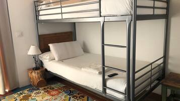 Un lit superposé avec une tête de lit en bois, un petit tabouret en bois et un tapis aux motifs colorés.