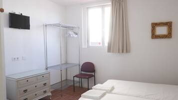 A hotel room with a bed, a chair, a TV, a drying rack, and a window with curtains.