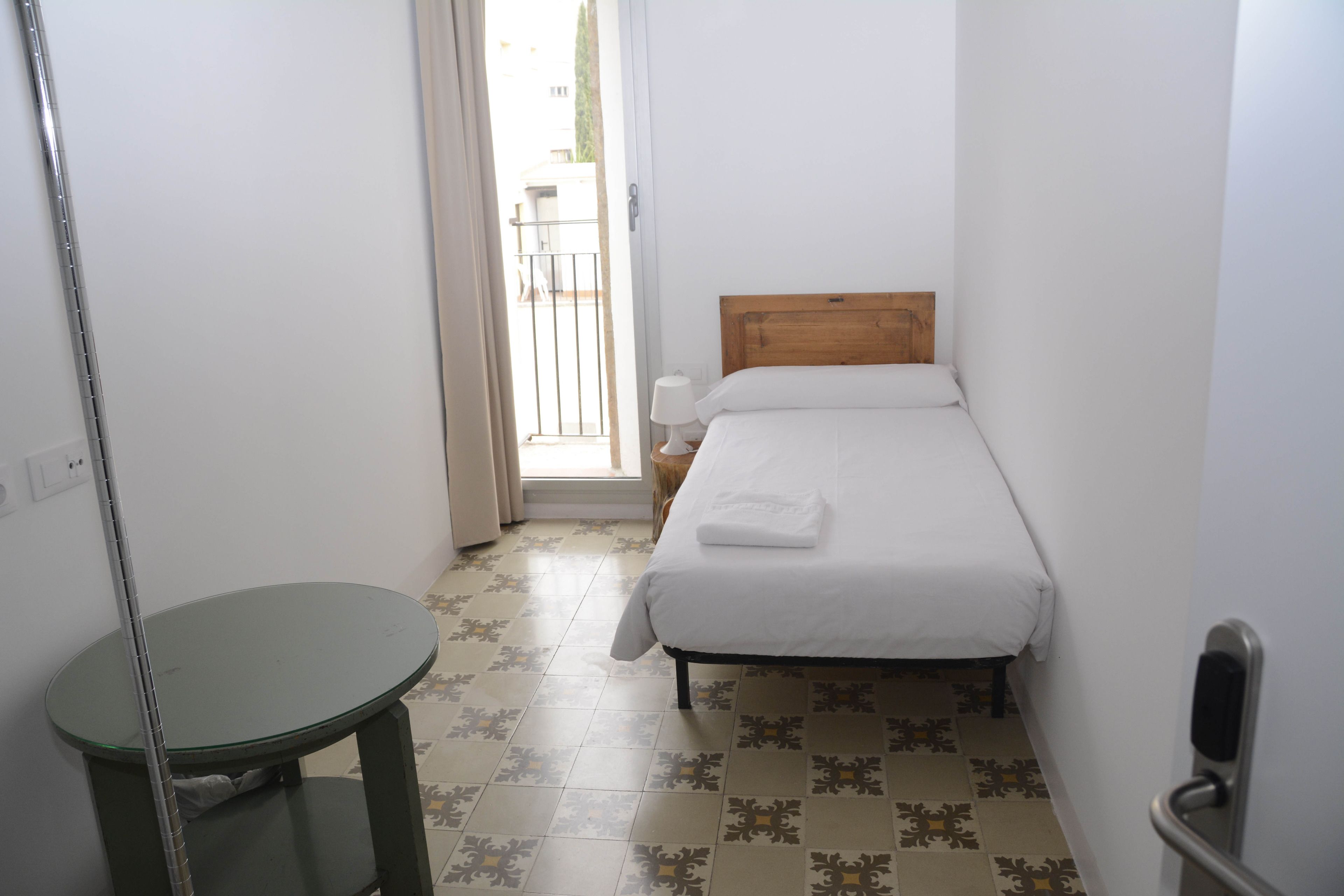 A small, clean room with a bed, a table, and a door leading outside.