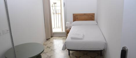 A small, clean room with a bed, a table, and a door leading outside.