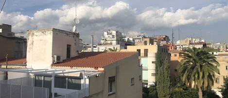 A cityscape with buildings, some with red-tiled roofs and others with flat designs. There are satellite dishes and antennas on rooftops.